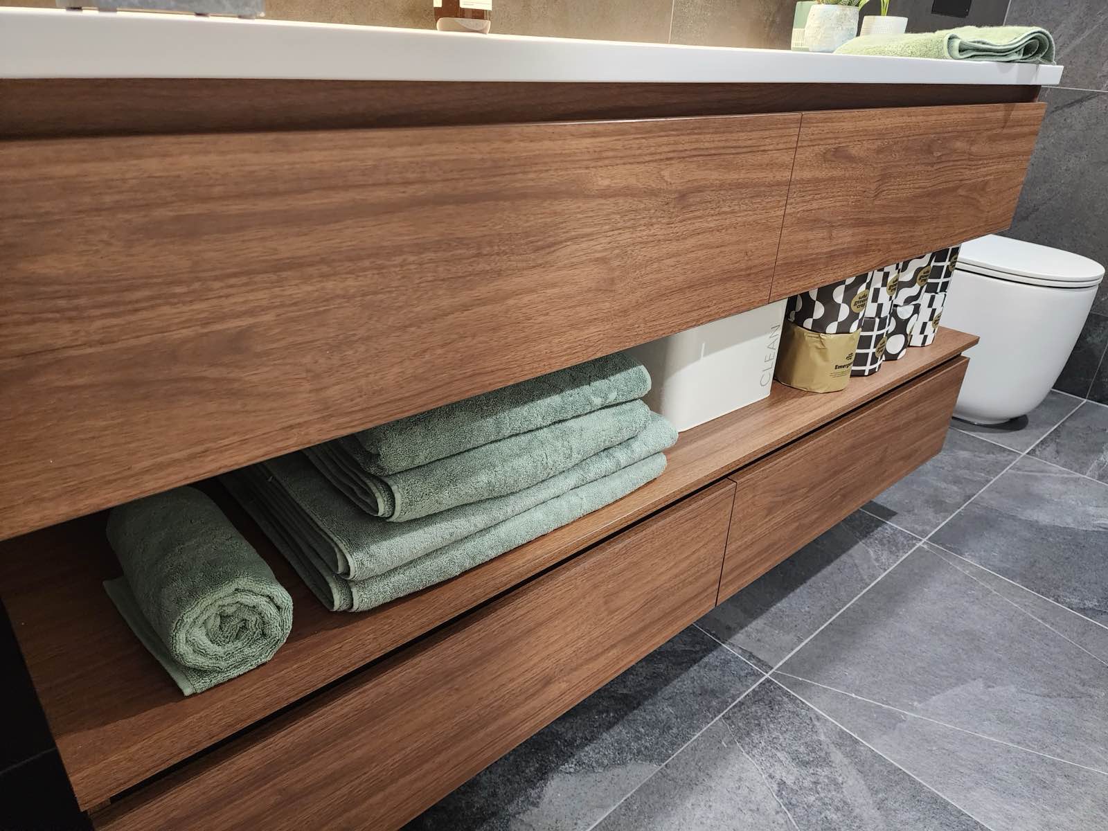 Now: the timber vanity's drawer and shelf edges, with towels stored on the open shelf