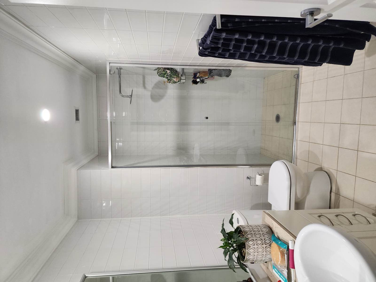 Main bathroom before renovation: chrome-framed sliding shower screen, beige floor tile and cream vanity