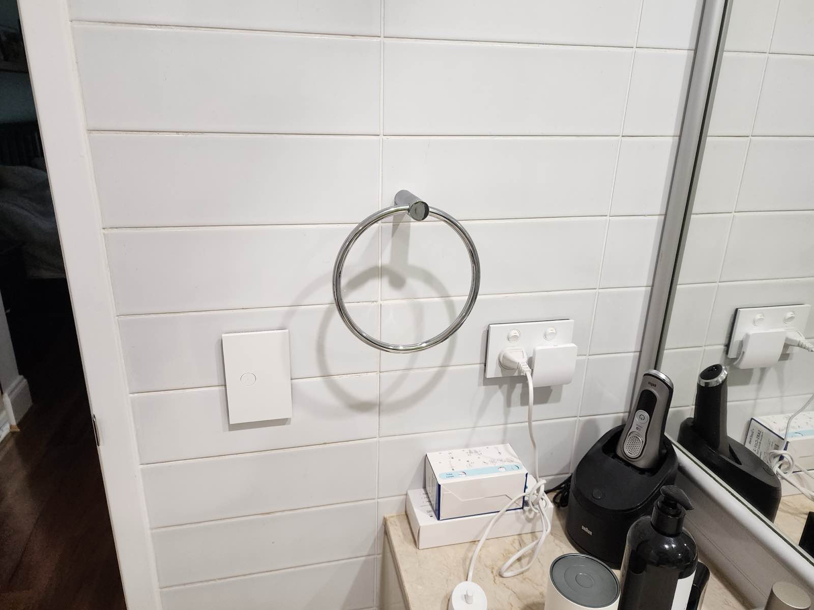 Before: a chrome towel ring between a light switch and a powerpoint on white subway tile