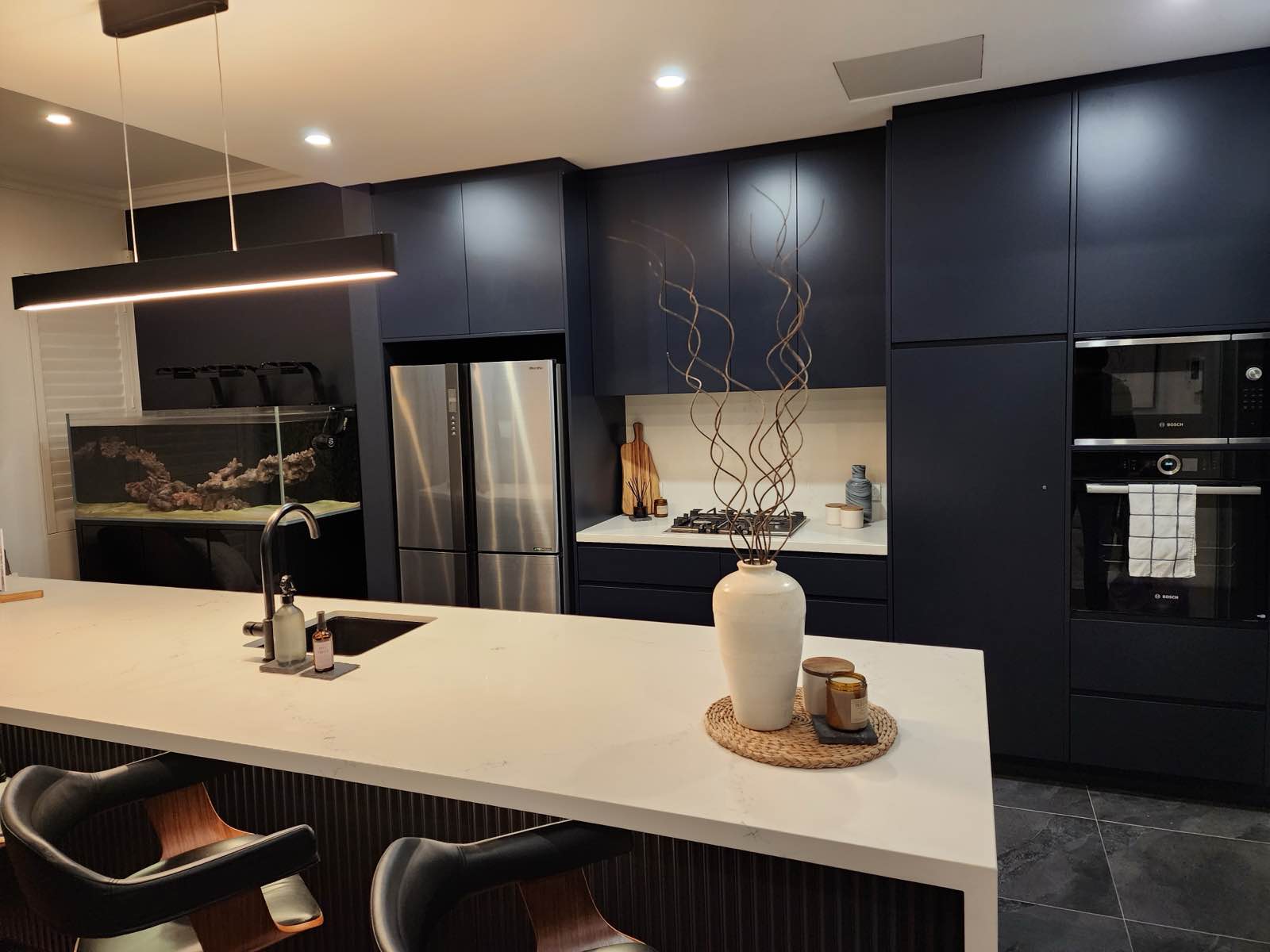 The rebuilt kitchen at night: navy cabinetry, stone island and linear pendant