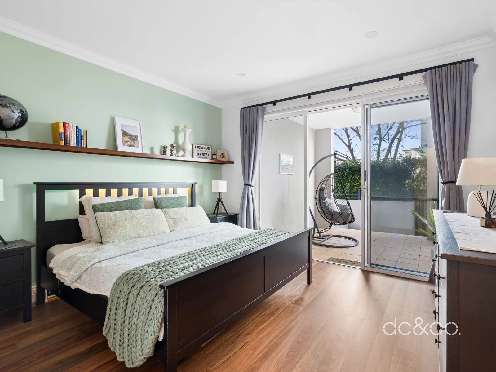 Main bedroom with sage feature wall, timber shelf and sliding door to its own patio