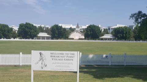 The Welcome to the Breakfast Point Village Green sign, picket fence and the Community Hall beyond